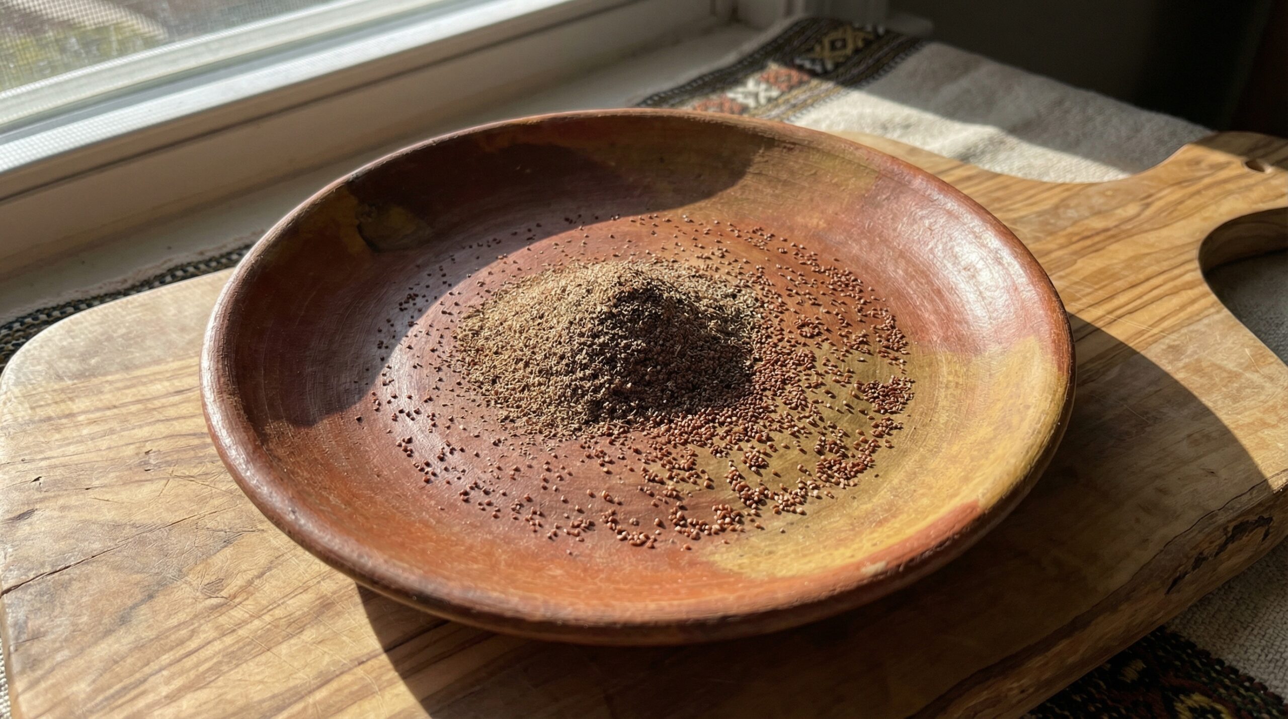 Dunkelbraunes Teffmehl und Teffkörner auf handgeformter Tonplatte auf Olivenholzbrett